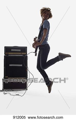 Stock Photography - A woman jumping while playing an electric guitar, studio shot, white background, back lit. Fotosearch