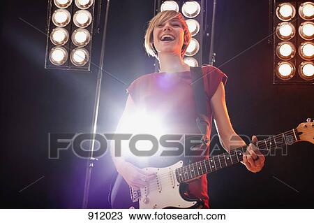 A woman playing electric guitar performing on stage View Large Photo Image Stock Image - A woman playing electric guitar performing on stage. Fotosearch
