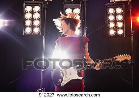 Stock Photo - A woman playing electric guitar performing on stage. Fotosearch