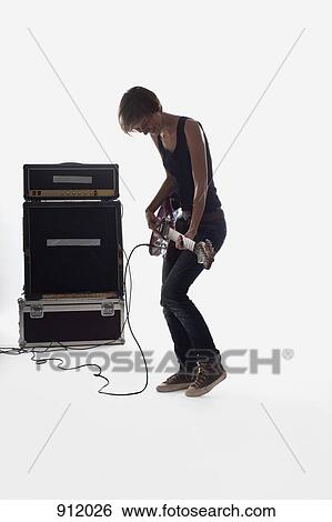 Stock Photograph - A woman playing electric guitar, studio shot, white background, back lit. Fotosearch