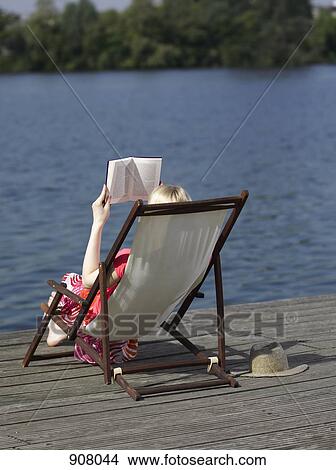 A woman reading in a reclining beach chair on a dock View Large Photo Image Picture - A woman reading in a reclining beach chair on a dock. Fotosearch