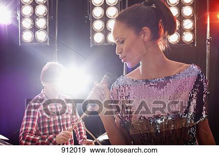 A woman singer accompanied by a man on drums performing on stage View Large Photo Image Stock Photo - A woman singer accompanied by a man on drums performing on stage. Fotosearch