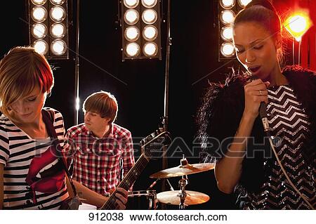A woman singer accompanied by a man on drums and a woman on guitar performing on stage View Large Photo Image Stock Photo - A woman singer accompanied by a man on drums and a woman on guitar performing on stage. Fotosearch