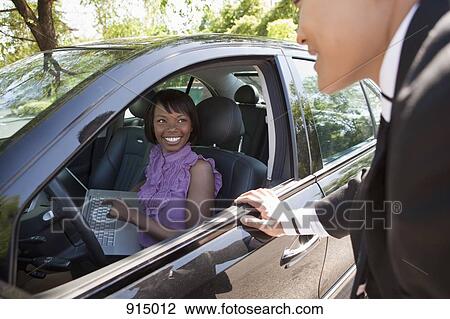 A woman sitting in a car holding a laptop talking with a man outside the car View Large Photo Image Stock Image - A woman sitting in a car holding a laptop talking with a man outside the car. Fotosearch