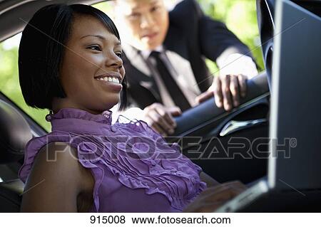 Stock Photo - A woman sitting in a car using a laptop while a man leans into the car. Fotosearch