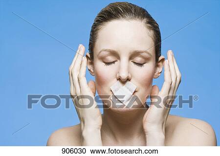 Stock Image - A woman with tape covering her mouth, gesturing in frustration. Fotosearch