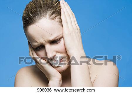 Stock Photograph - A woman with tape covering her mouth, holding her head in frustration. Fotosearch