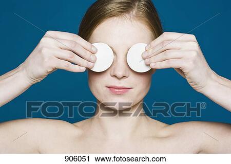 Stock Image - A woman with two cotton pads held up over her eyes. Fotosearch