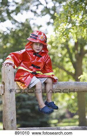 A young boy in a firefighter costume sitting on a fence View Large Photo Image Stock Image - A young boy in a firefighter costume sitting on a fence. Fotosearch