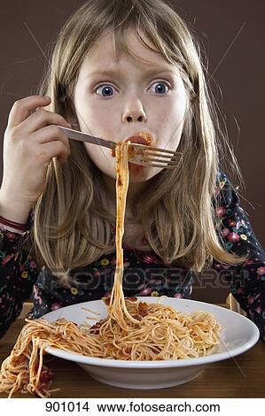 Picture - A young girl eating spaghetti messily, studio shot. Fotosearch