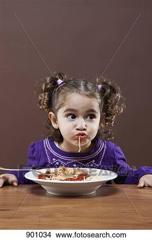 Picture - A young girl eating spaghetti, studio shot. Fotosearch