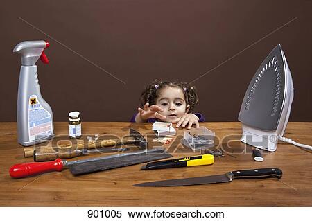 A young girl reaching onto a table of dangerous objects, studio shot View Large Photo Image Stock Photography - A young girl reaching onto a table of dangerous objects, studio shot. Fotosearch