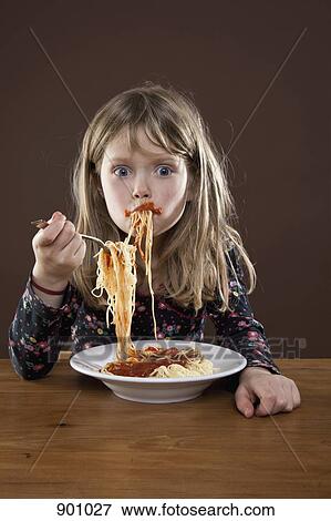 Stock Photo - A young girl shoving spaghetti messily into her mouth, studio shot. Fotosearch