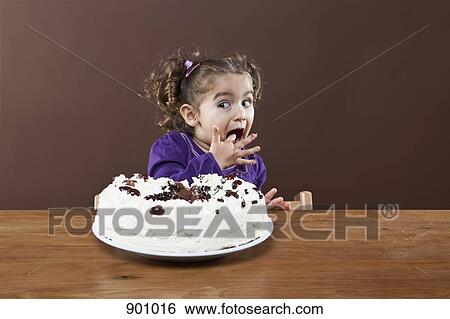 Stock Photograph - A young girl sneaking a taste of a frosted cake, studio shot. Fotosearch