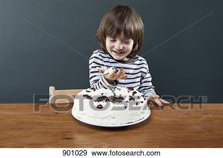 Stock Photo - A young smiling boy holding a handful of cake, studio shot. Fotosearch