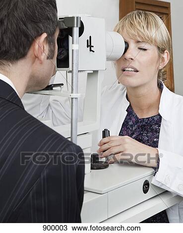 Stock Image - An ophthalmologist using a slit-lamp biomicroscope to examine a patient. Fotosearch
