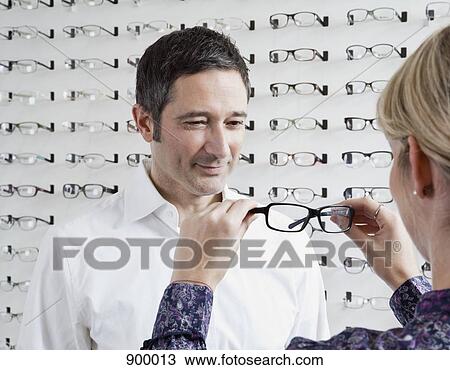 An optician holding up glasses to a man in an eyewear store View Large Photo Image Stock Image - An optician holding up glasses to a man in an eyewear store. Fotosearch