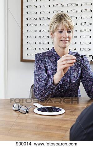 An optician holding up glasses to a customer in an eyewear store View Large Photo Image Picture - An optician holding up glasses to a customer in an eyewear store. Fotosearch