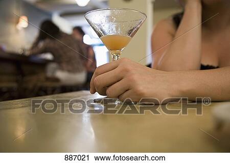 Stock Image - Detail of a woman holding a drink at a bar. Fotosearch