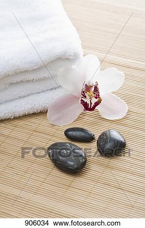 Picture - Folded towels, hot stone therapy stones and an orchid arranged on a Tatami mat. Fotosearch