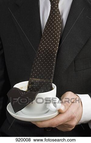 Man holding a cup of coffee with tie floating in it View Large Photo Image Stock Photo - Man holding a cup of coffee with tie floating in it. Fotosearch
