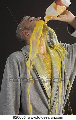 Stock Photography - Man in a bathrobe pouring orange juice into his mouth and spilling it. Fotosearch