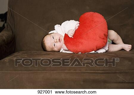 Stock Image - A baby lying on her side embracing a heart shaped pillow. Fotosearch