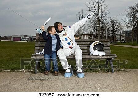 A boy holding a model rocket sitting with an astronaut on a park bench View Large Photo Image Stock Photo - A boy holding a model rocket sitting with an astronaut on a park bench. Fotosearch