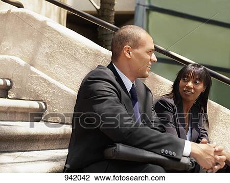 Stock Image - A businessman and businesswoman sitting on some stairs and having a discussion. Fotosearch
