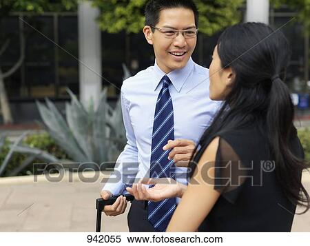 A businessman holding a rolling suitcase handle and a businesswoman talking View Large Photo Image Stock Photography - A businessman holding a rolling suitcase handle and a businesswoman talking. Fotosearch