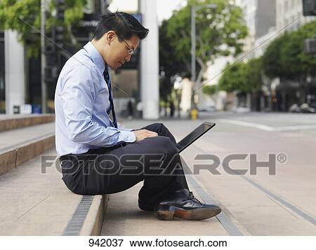 A businessman sitting cross-legged on some steps, using a laptop View Large Photo Image Stock Photo - A businessman sitting cross-legged on some steps, using a laptop. Fotosearch