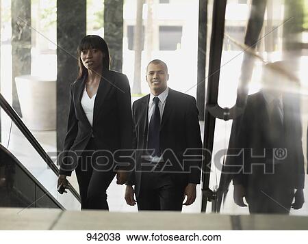 A businesswoman and businessman walking up stairs in an office building View Large Photo Image Stock Photo - A businesswoman and businessman walking up stairs in an office building. Fotosearch