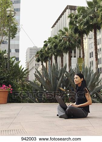 A businesswoman sitting cross-legged in the courtyard of an office complex, using a laptop View Large Photo Image Stock Image - A businesswoman sitting cross-legged in the courtyard of an office complex, using a laptop. Fotosearch