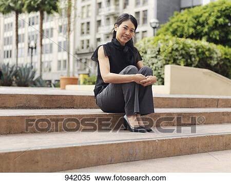 Stock Photography - A businesswoman sitting on the outdoor steps of an office complex. Fotosearch