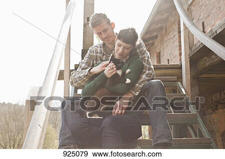 A couple holding and petting a cat View Large Photo Image Stock Photo - A couple holding and petting a cat. Fotosearch