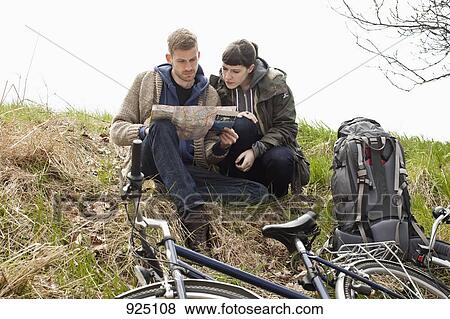 Stock Photo - A couple sitting on a hill next to their bicycles looking at a map. Fotosearch