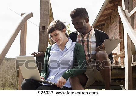 Stock Image - A couple sitting on a staircase, looking at a laptop together. Fotosearch