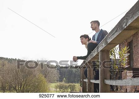 A couple standing on a balcony looking into the distance View Large Photo Image Stock Photo - A couple standing on a balcony looking into the distance. Fotosearch