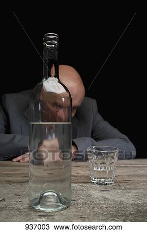 Stock Image - A drunk and depressed businessman with a bottle of vodka and an empty glass. Fotosearch