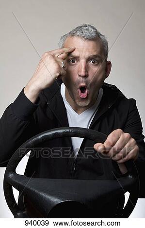 A frustrated man gesturing behind a car steering wheel View Large Photo Image Stock Photo - A frustrated man gesturing behind a car steering wheel. Fotosearch