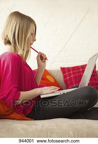 Stock Image - A girl sitting with a laptop on a sofa. Fotosearch