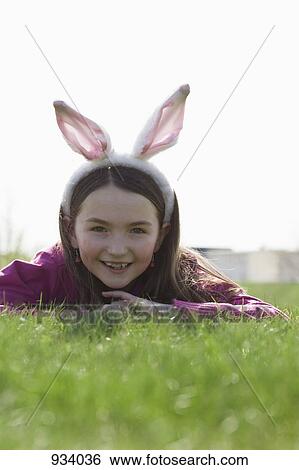 Stock Photograph - A girl wearing rabbit ears and lying down on grass. Fotosearch