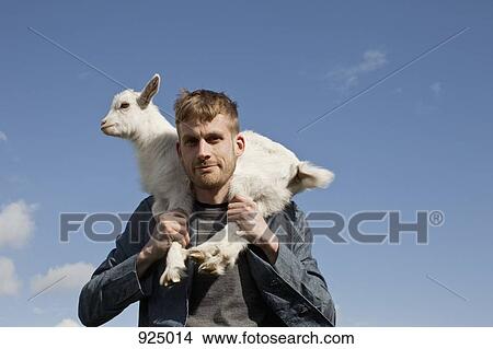 Picture - A man carrying a kid goat on his shoulders. Fotosearch
