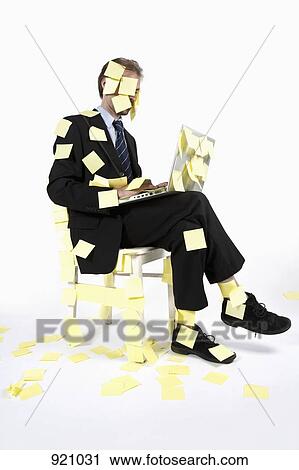 Stock Image - A man covered in blank adhesive notes while sitting and using a laptop. Fotosearch