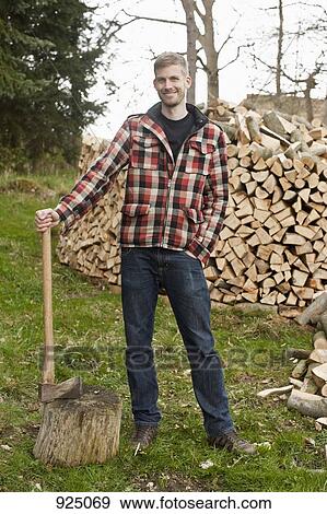 Stock Photo - A man holding an axe, standing in front of a wood pile. Fotosearch