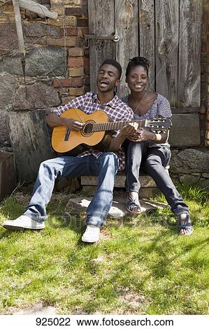 Stock Image - A man playing an acoustic guitar and singing with his girlfriend. Fotosearch