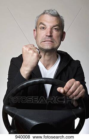 A man shaking his fist behind a car steering wheel View Large Photo Image Stock Photo - A man shaking his fist behind a car steering wheel. Fotosearch