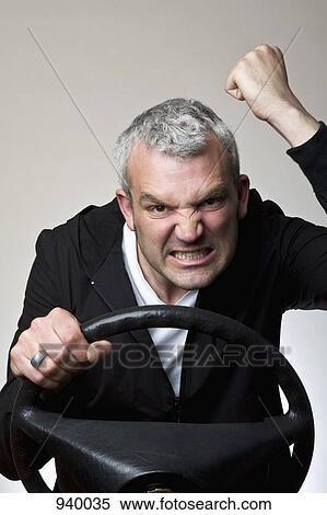 A man shaking his fist behind a car steering wheel View Large Photo Image Stock Photography - A man shaking his fist behind a car steering wheel. Fotosearch