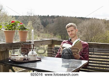 A man sitting at a table on a balcony reading View Large Photo Image Stock Photograph - A man sitting at a table on a balcony reading. Fotosearch
