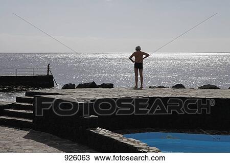 A man standing by a swimming pool next to the sea View Large Photo Image Stock Image - A man standing by a swimming pool next to the sea. Fotosearch